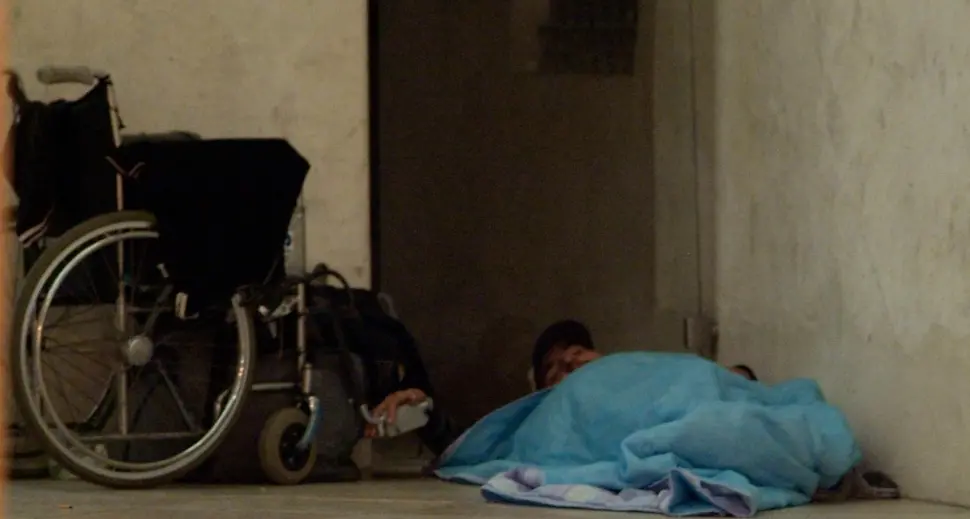 Il clochard disabile che dorme tenendo per mano la sua carrozzina