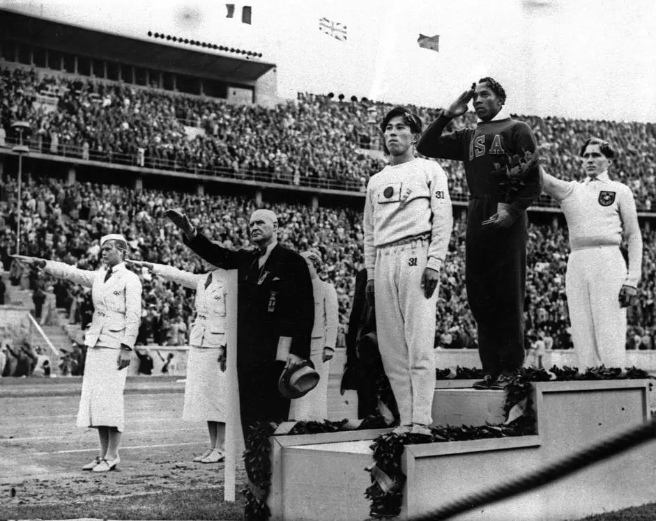 FILE - In this Aug. 11, 1936 file photo, Olympic broad jump medalists salute during the medals ceremony at the Summer Olympics in Berlin. From left on podium are: bronze medalist Jajima of Japan, gold medalist Jesse Owens of the United States and silver medalist Lutz Long of Germany. Long and German Olympic officials give the Nazi salute, while Owens gives a traditional salute. It is \\\"difficult\\\" for IOC President Thomas Bach to accept that a gold medal won by Jesse Owens at the 1936 Olympics will go on auction and possibly be bought by a private collector. The medal, one of four golds that Owens won at the Berlin Games in front of Adolf Hitler, is \\\"a part of world heritage,\\\" Bach said Wednesday, Nov. 13, 2013. (AP Photo/File)